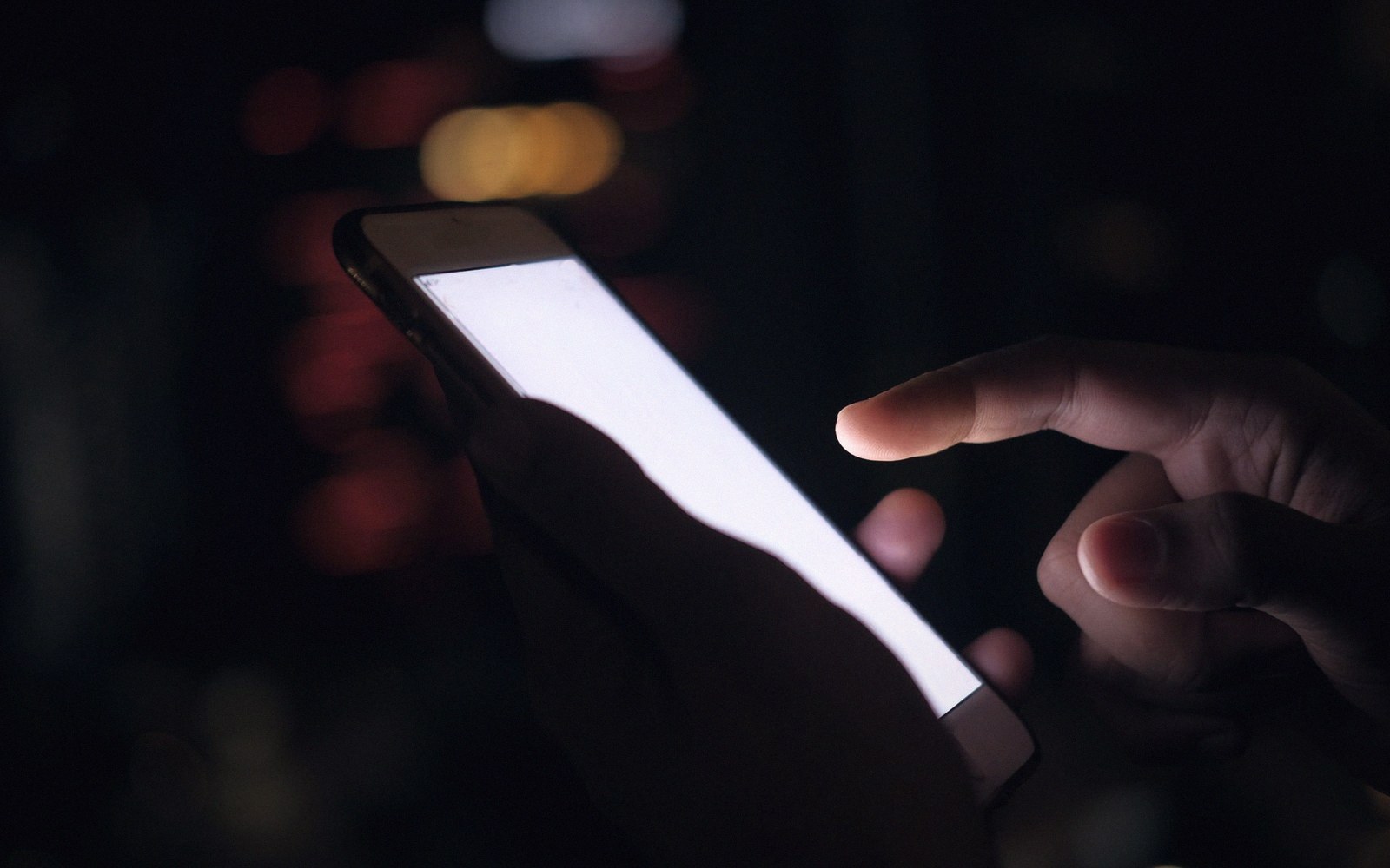 A finger touches a smartphone's glowing white screen in a dark setting