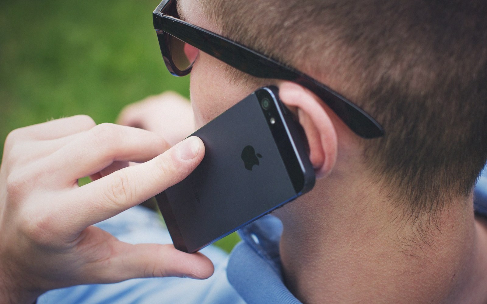 Man wearing sunglasses holds an iPhone to his ear outdoors