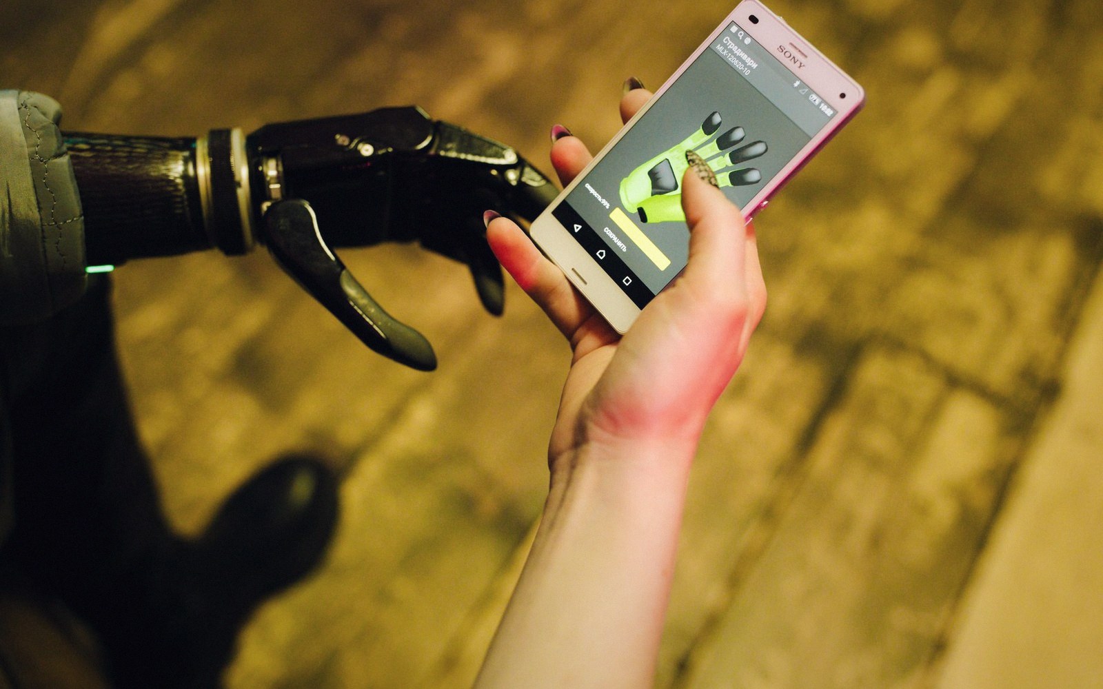 A robotic prosthetic hand reaches toward a smartphone held by a human hand