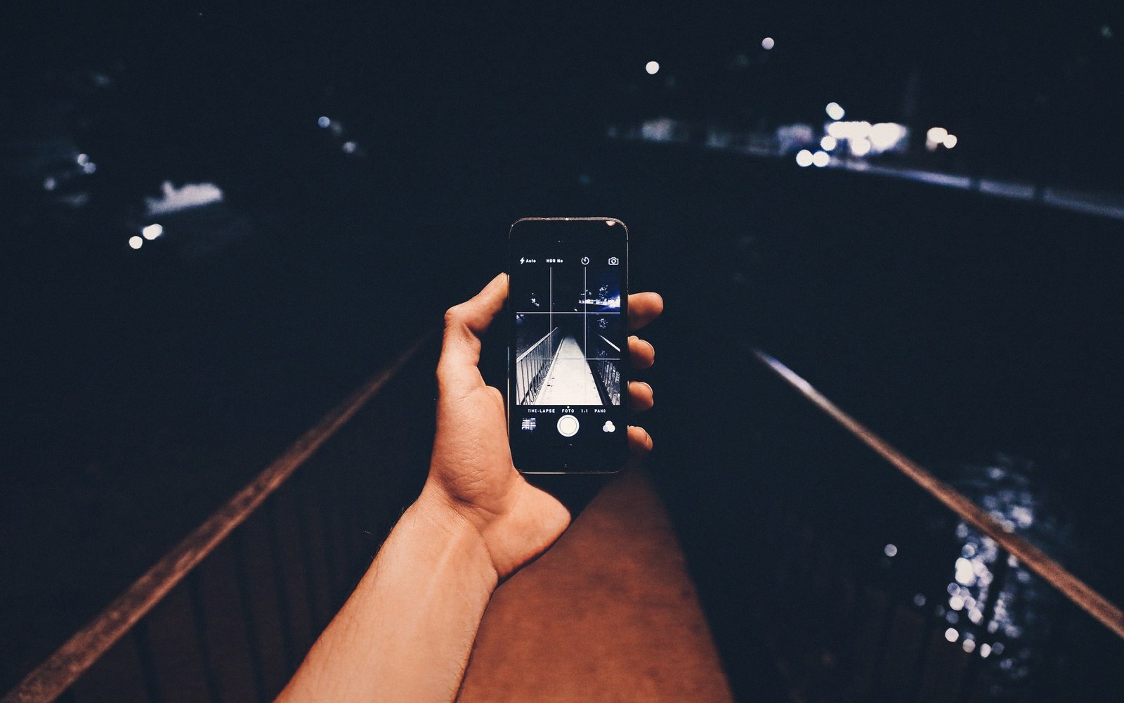 A hand holds up a smartphone photographing a bridge railing at night