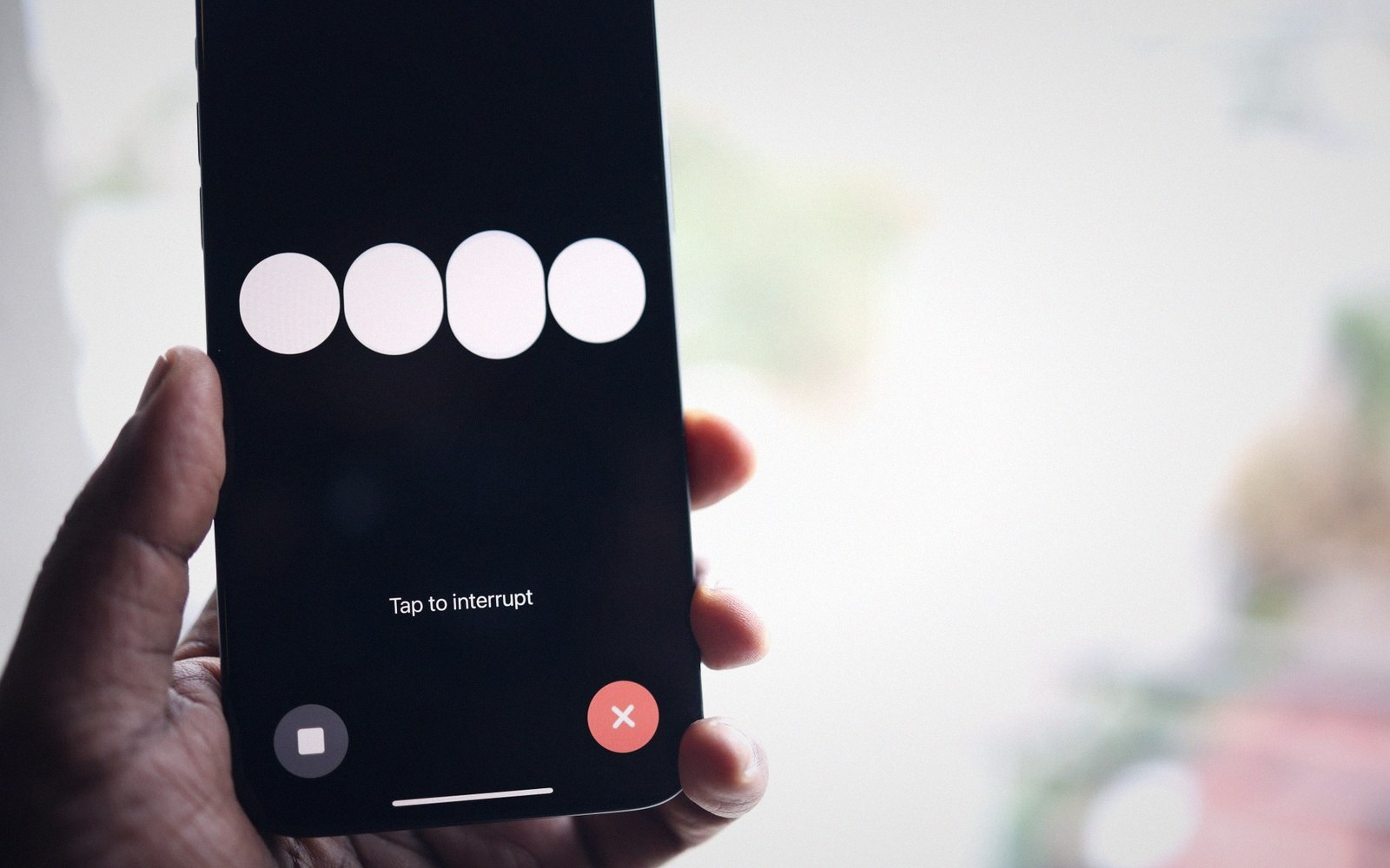 A hand holds a smartphone showing a voice assistant screen with "Tap to interrupt" text